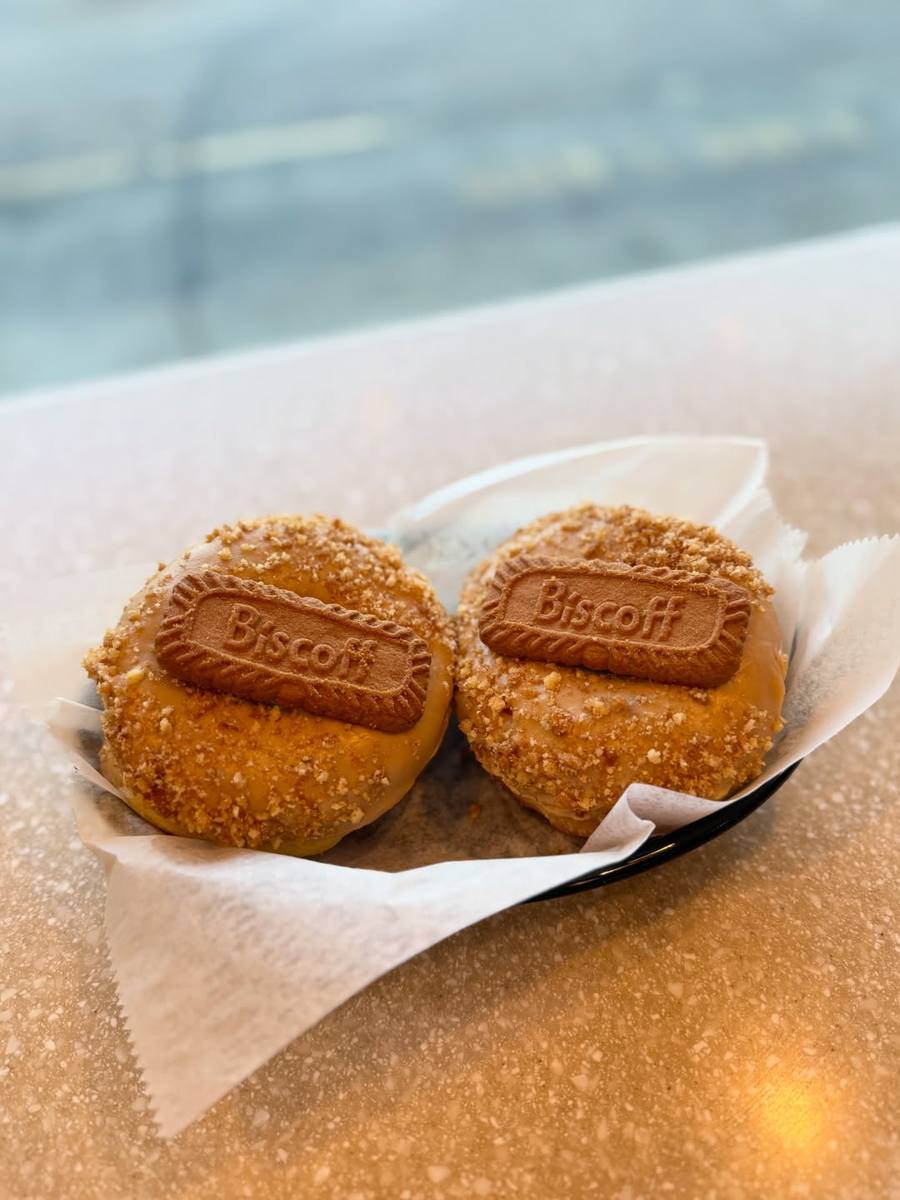 Two Biscoff donuts sitting on parchment in a black basket on the counter, backlit by the shop window.