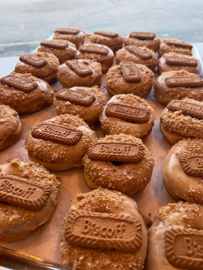 A full sheet tray of Biscoff donuts, each glazed in cookie butter, dusted with cookie crumb and finished with a whole Biscoff biscuit.