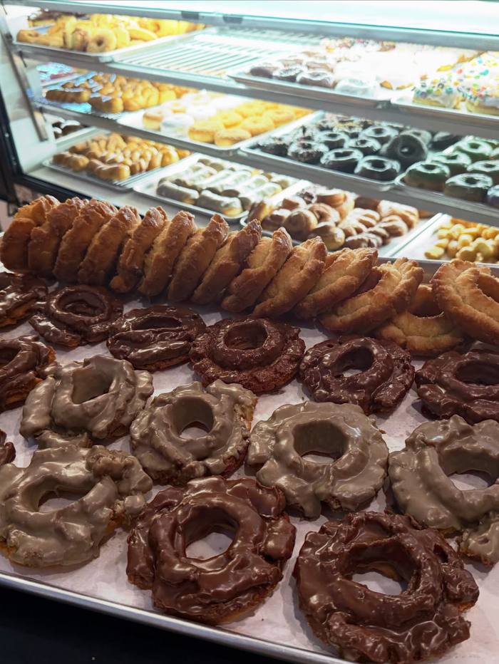 Milkee's display case stacked with maple and chocolate old-fashioned rings, rows of golden twists, glazed rings, long johns and sprinkle donuts.