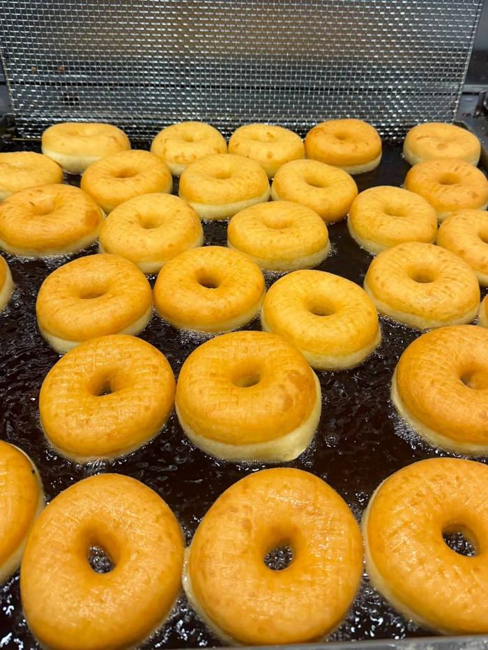 Dozens of donuts floating in hot oil in the fryer, their edges turned deep golden and the tops still pale.